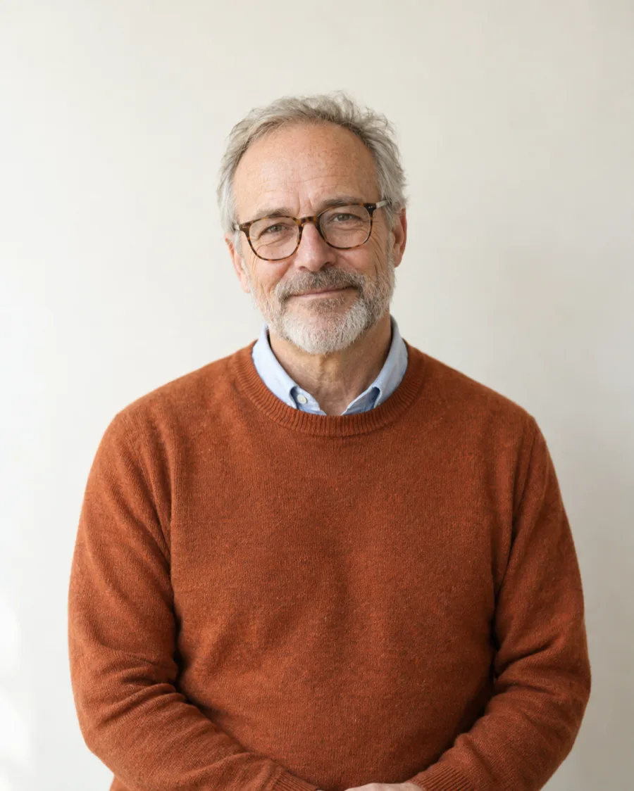 Dr. Tom Hollis standing against a warm white backdrop in a rust sweater
