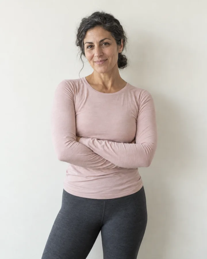 Ines Varga, a teacher in her forties in a chalk pink top, arms crossed, half smiling